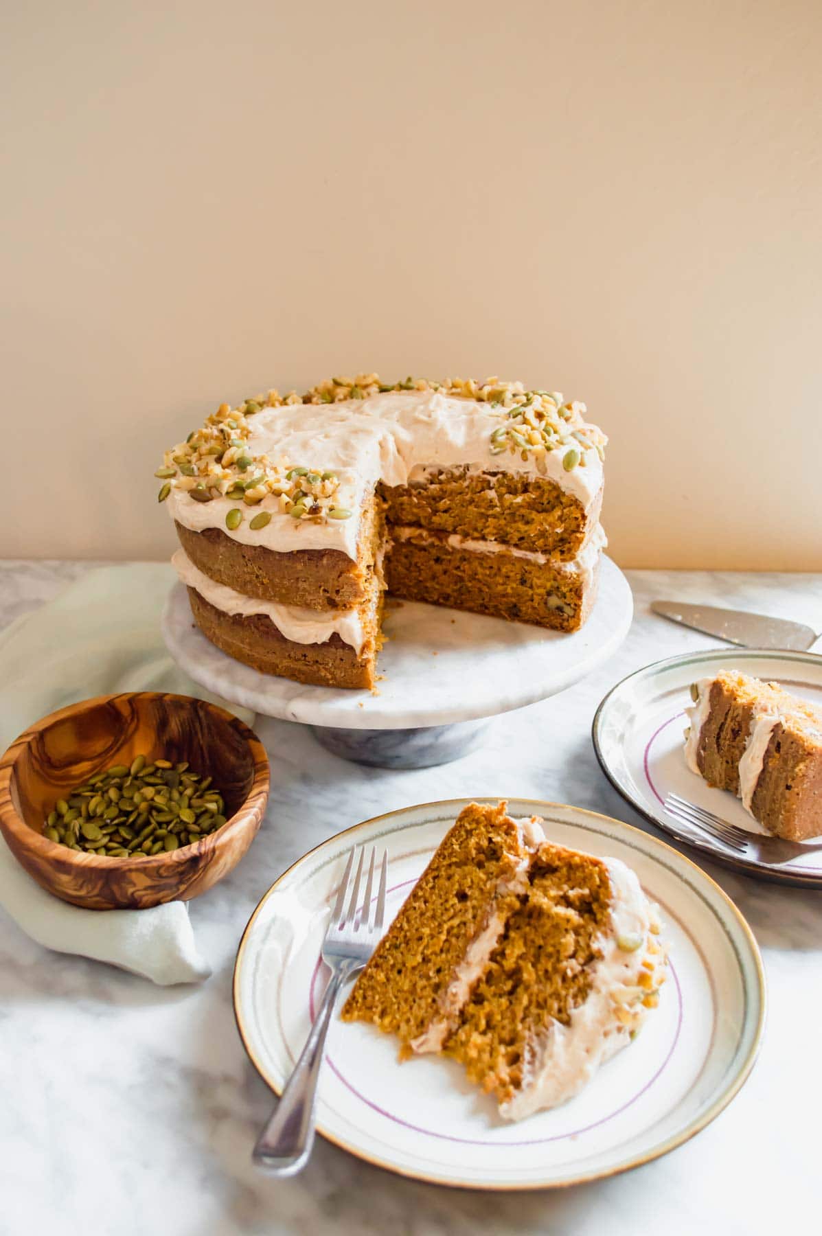 Slices of Carrot Cake with Chai Spiced Frosting with cake on cake stand and pepitas.