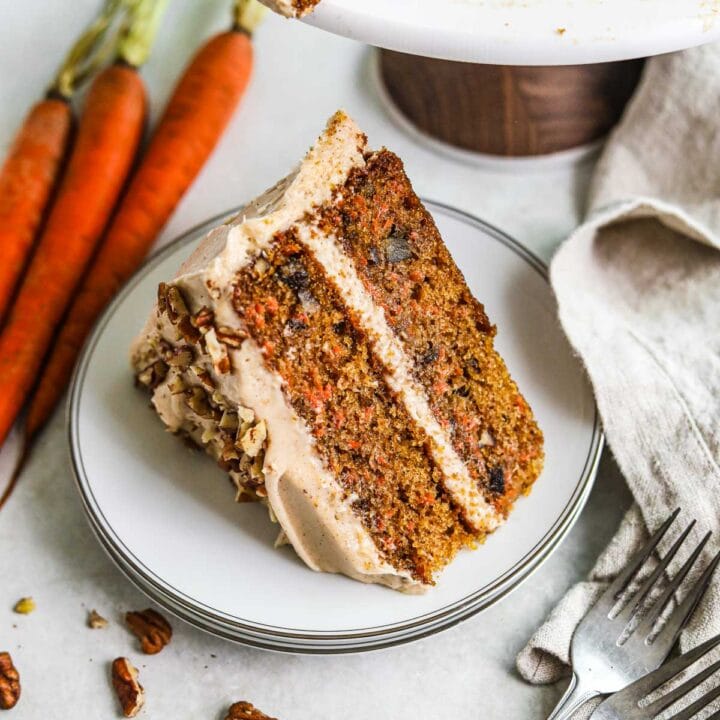 Moist and tender layered carrot cake with pecans and chai spiced cream cheese frosting on a plate.
