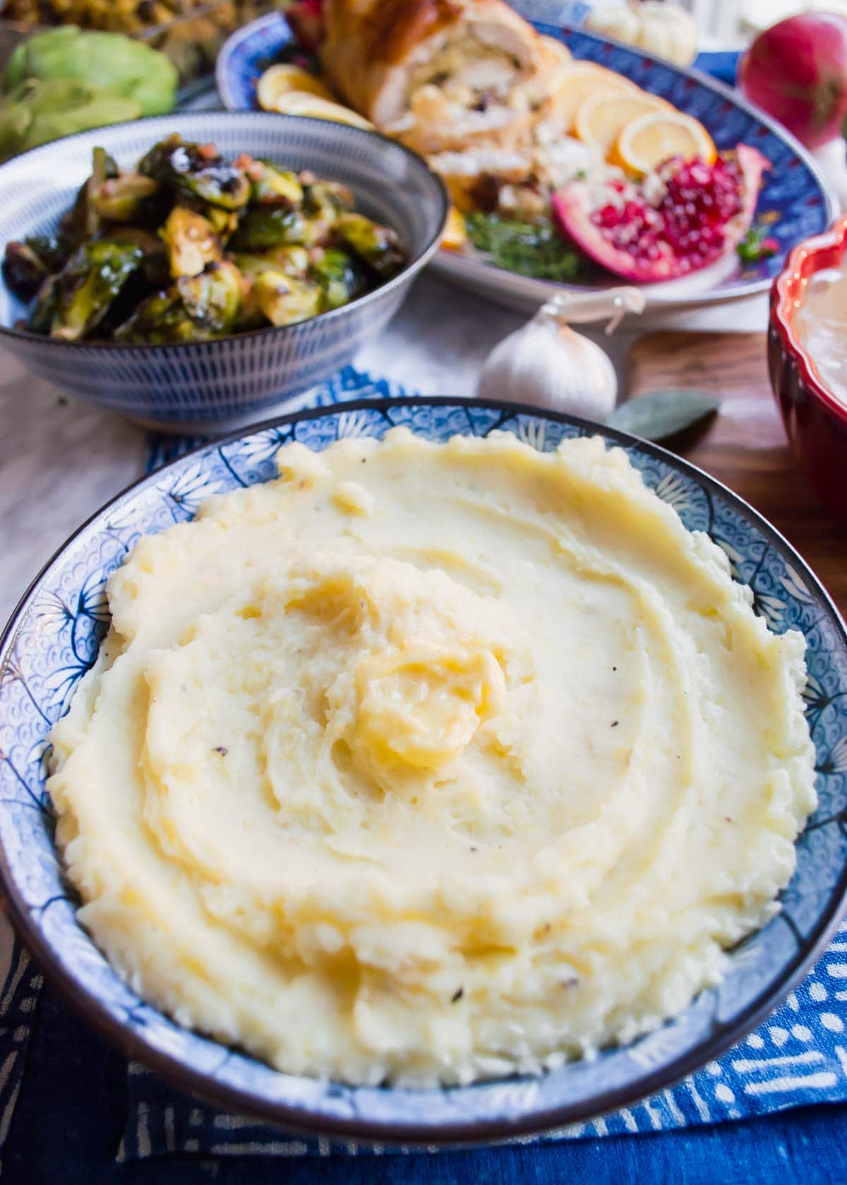 Roasted Garlic Mashed Potatoes in bowl with Thanksgiving sides in background.