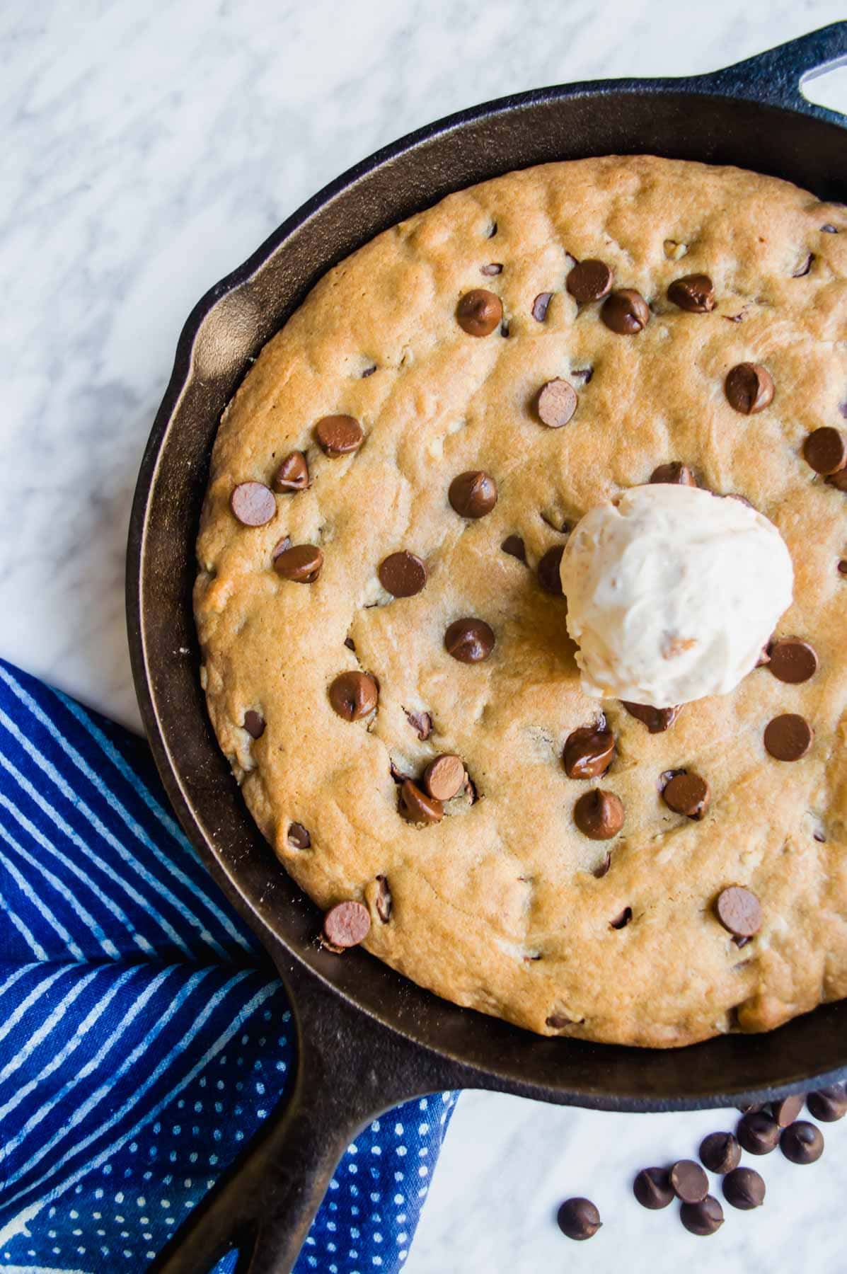 Chocolate Chip Skillet Cookie in cast iron skillet with ice cream on top flatlay.