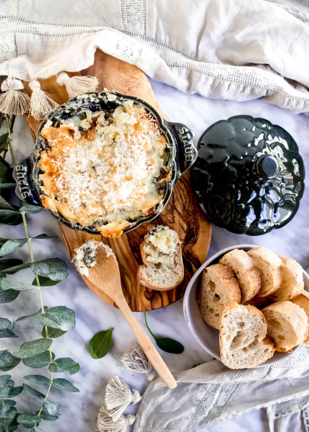 Creamy Spinach and Artichoke Dip in serving bowl with spoon and bread flatlay.