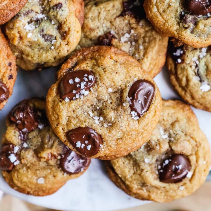Crispy chewy chocolate chip walnut cookies stacked on a marble cake stand.