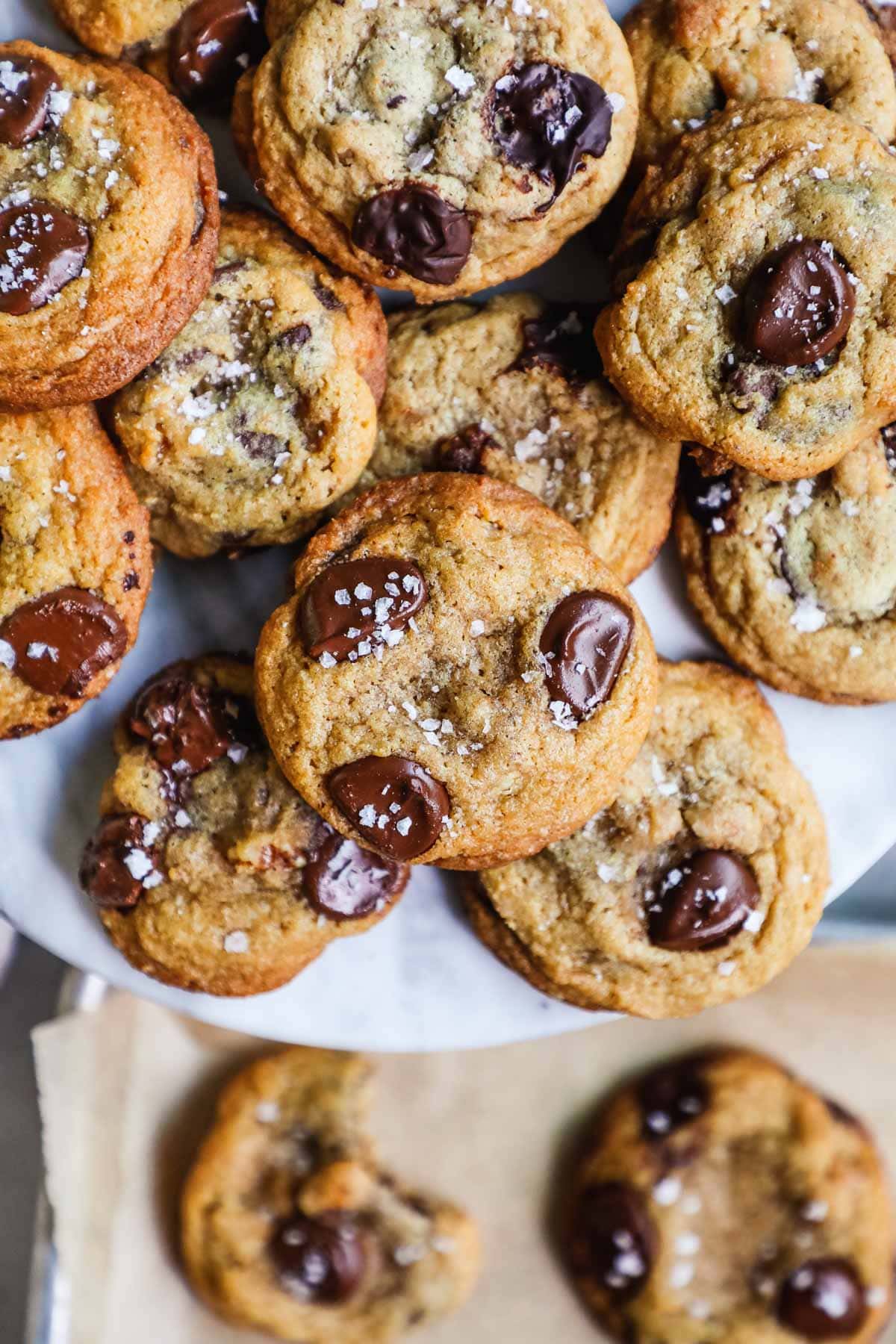 Crispy chewy chocolate chip walnut cookies stacked on a marble cake stand.