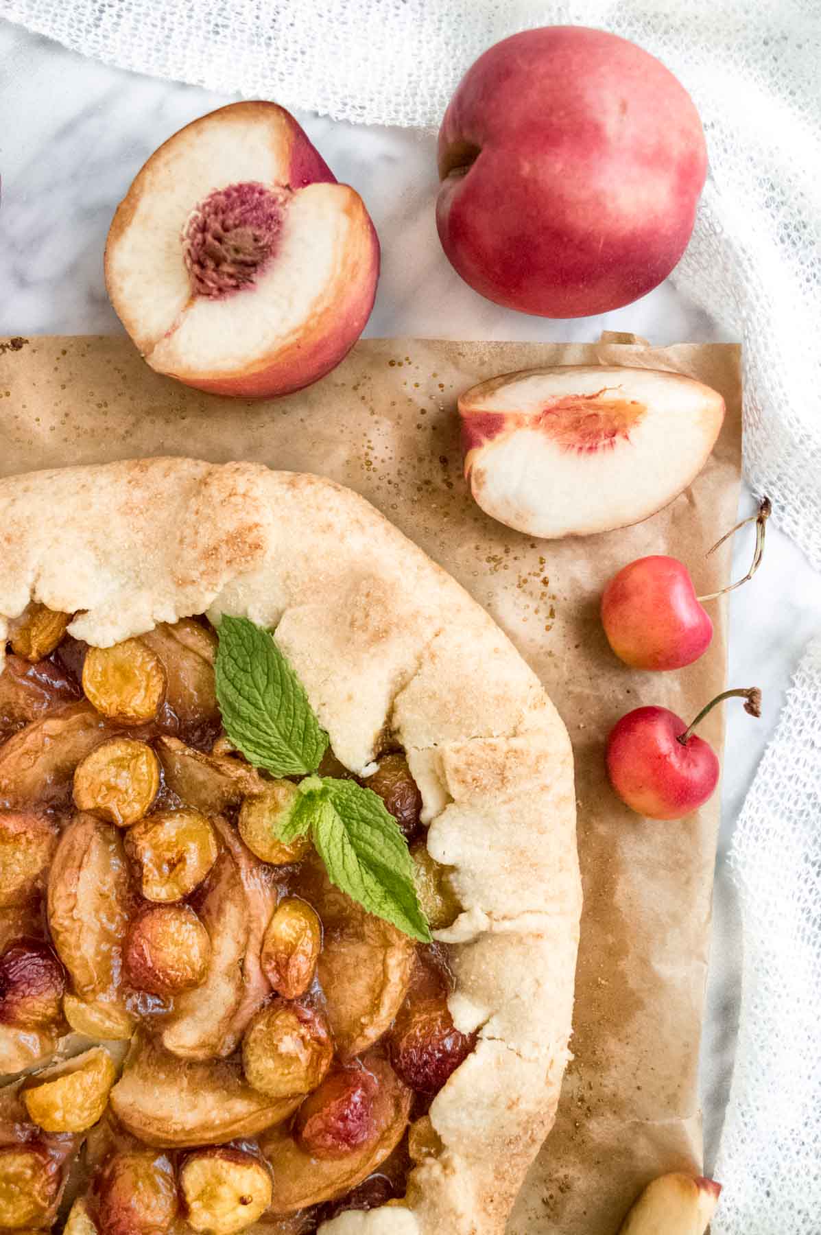 White Peach and Cherry Galette on parchment paper with sliced peaches flatlay.