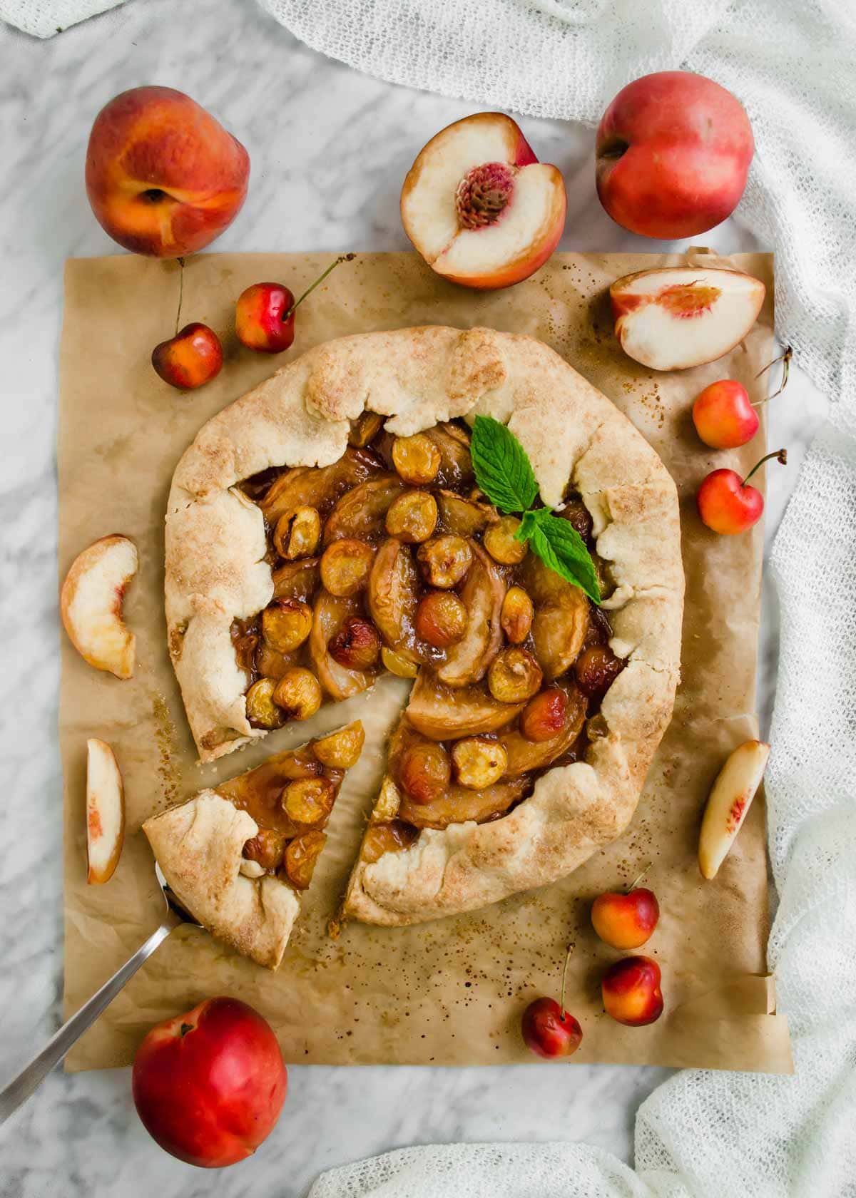 White Peach and Cherry Galette on parchment paper with sliced peaches and cherries flatlay.