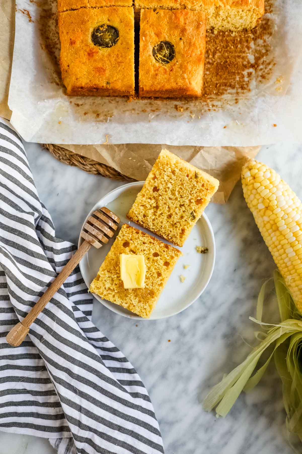 Jalapeño Cheddar Cornbread with Miso sliced on plate with butter and corn husk.