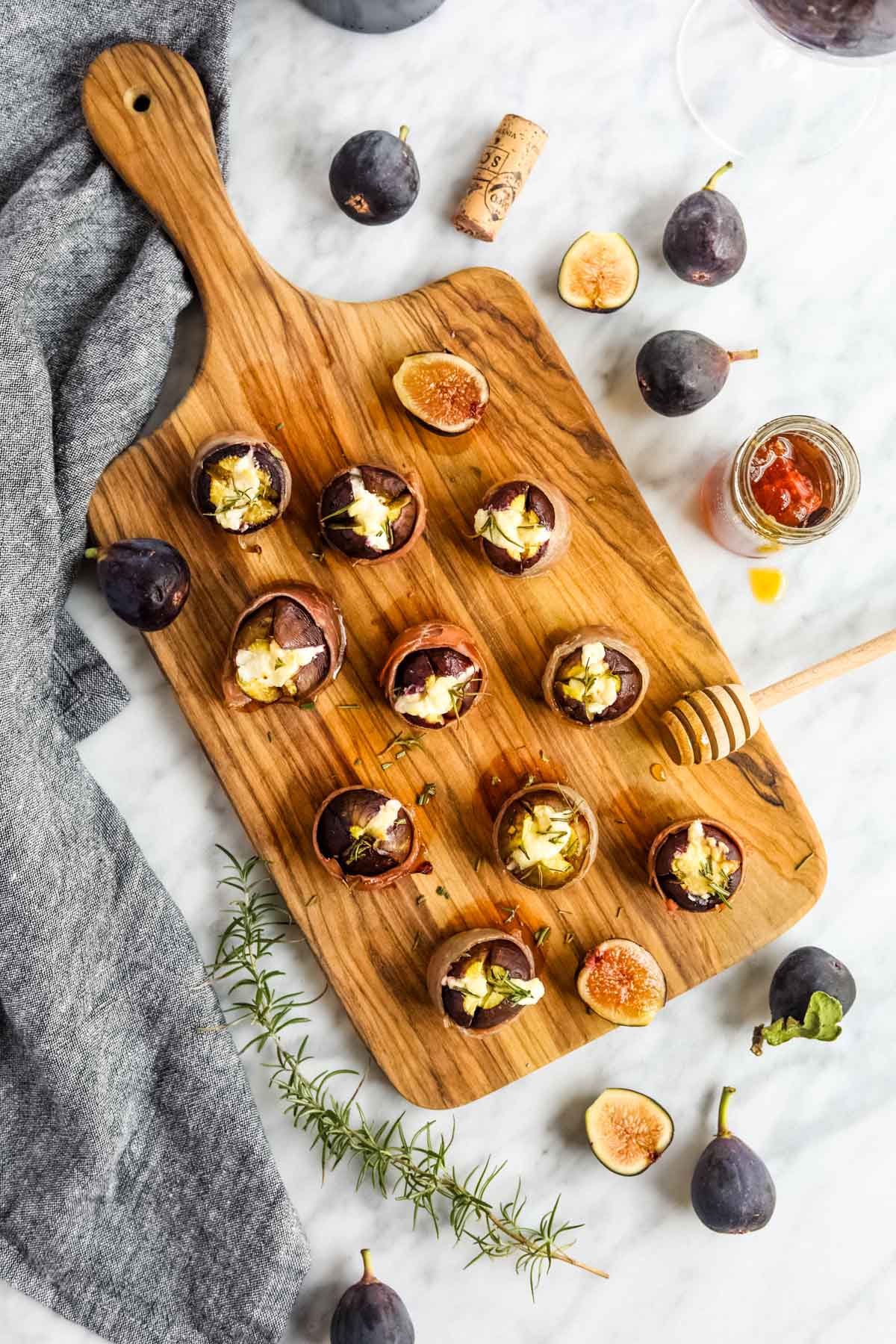 Prosciutto Wrapped Figs with Goat Cheese on cutting board with honey flatlay.