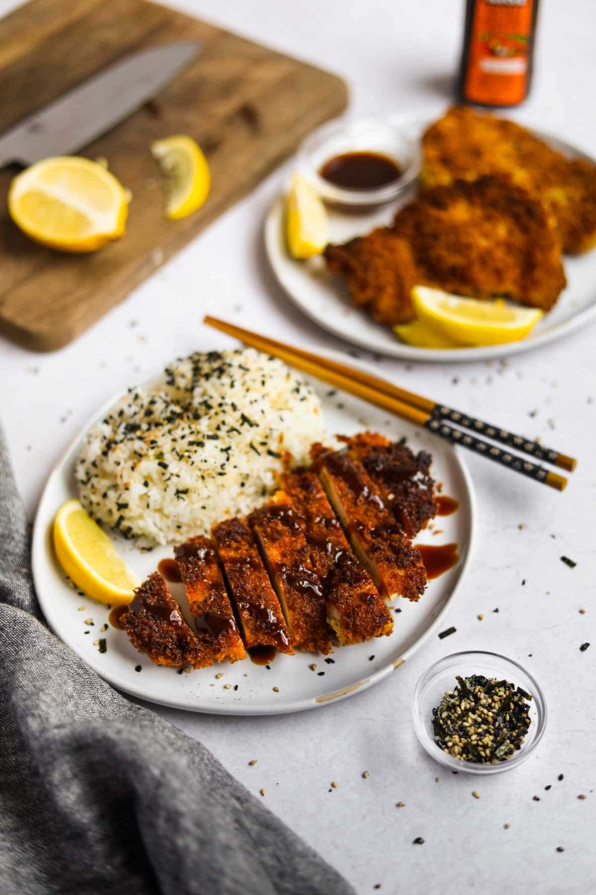 Chicken Katsu (Japanese Chicken Cutlet) on a plate with rice with lemon slices and and furikake.