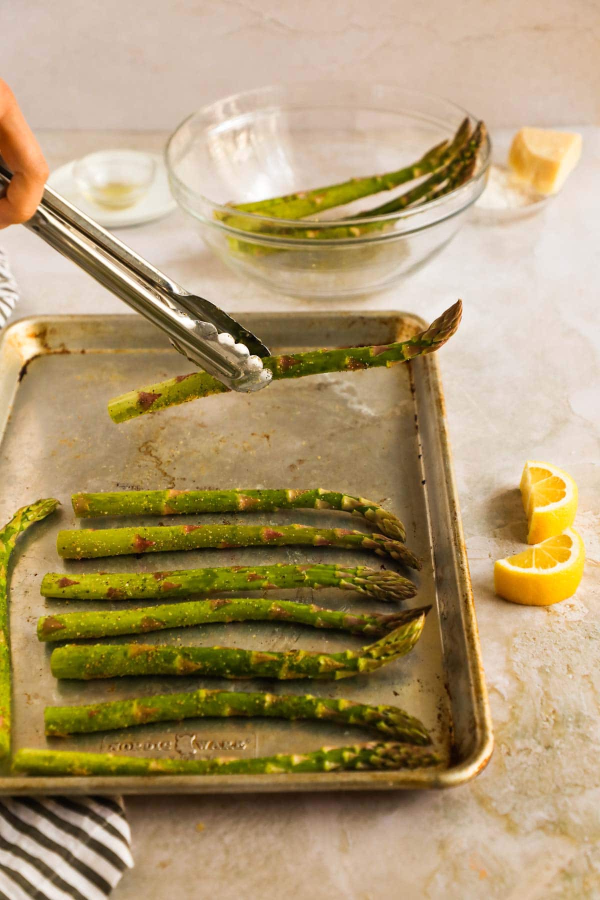 Tongs placing asparagus on Nordicware baking sheet pan.
