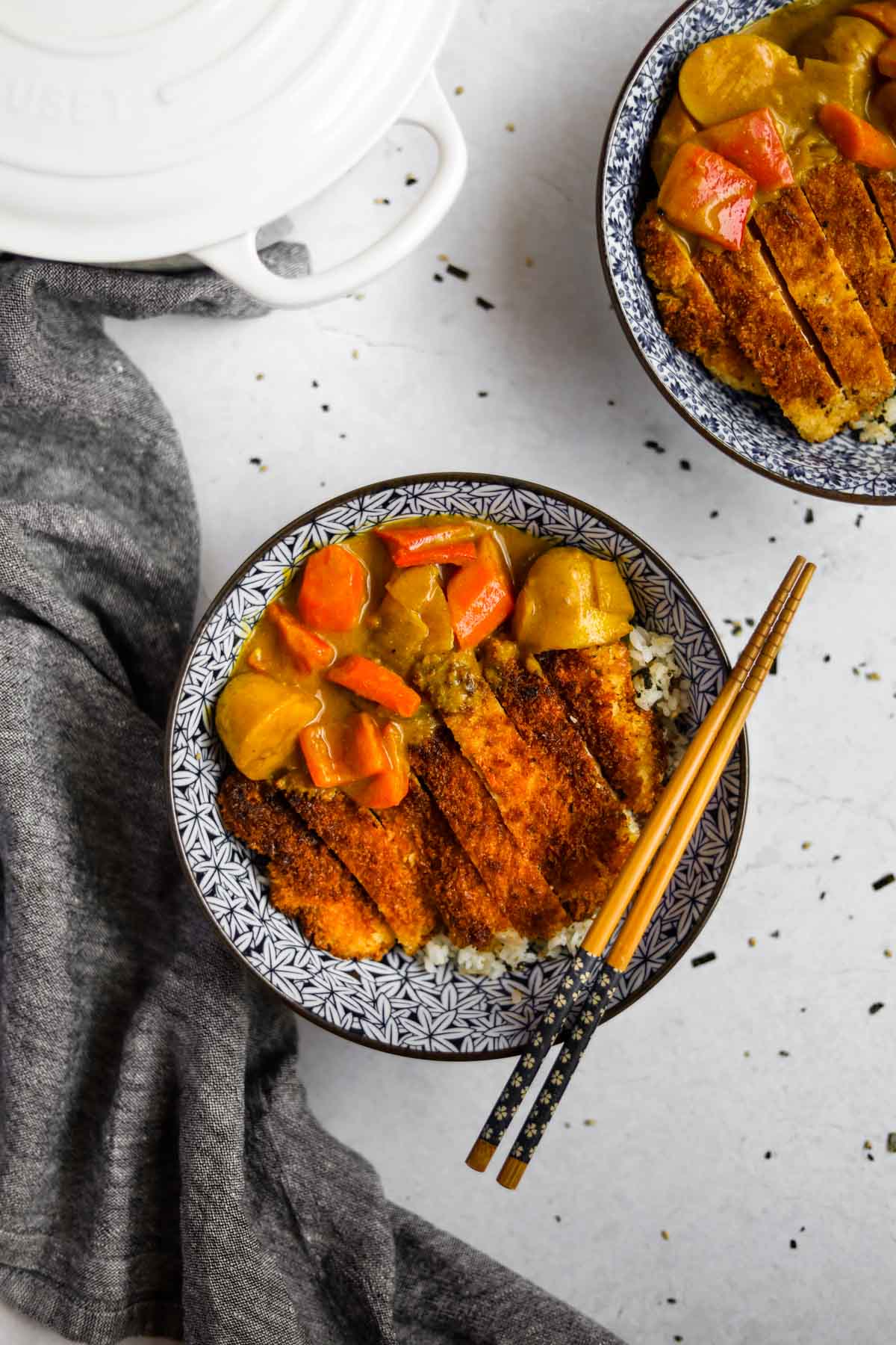 Overhead shot of Chicken Katsu Curry in a blue Japanese porcelain bowl with blue and wood bamboo chopsticks and a white Le Creuset dutch oven