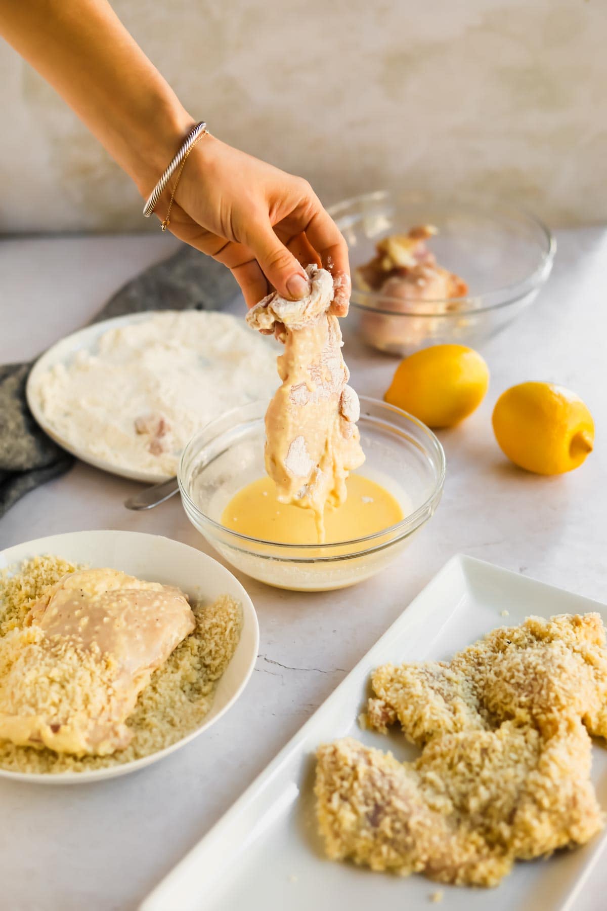 Raw chicken being dipped into egg mixture with lemons, flour, and panko