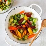 Brussel Sprouts and Carrots in a white Le Creuset braiser with a wooden spoon.