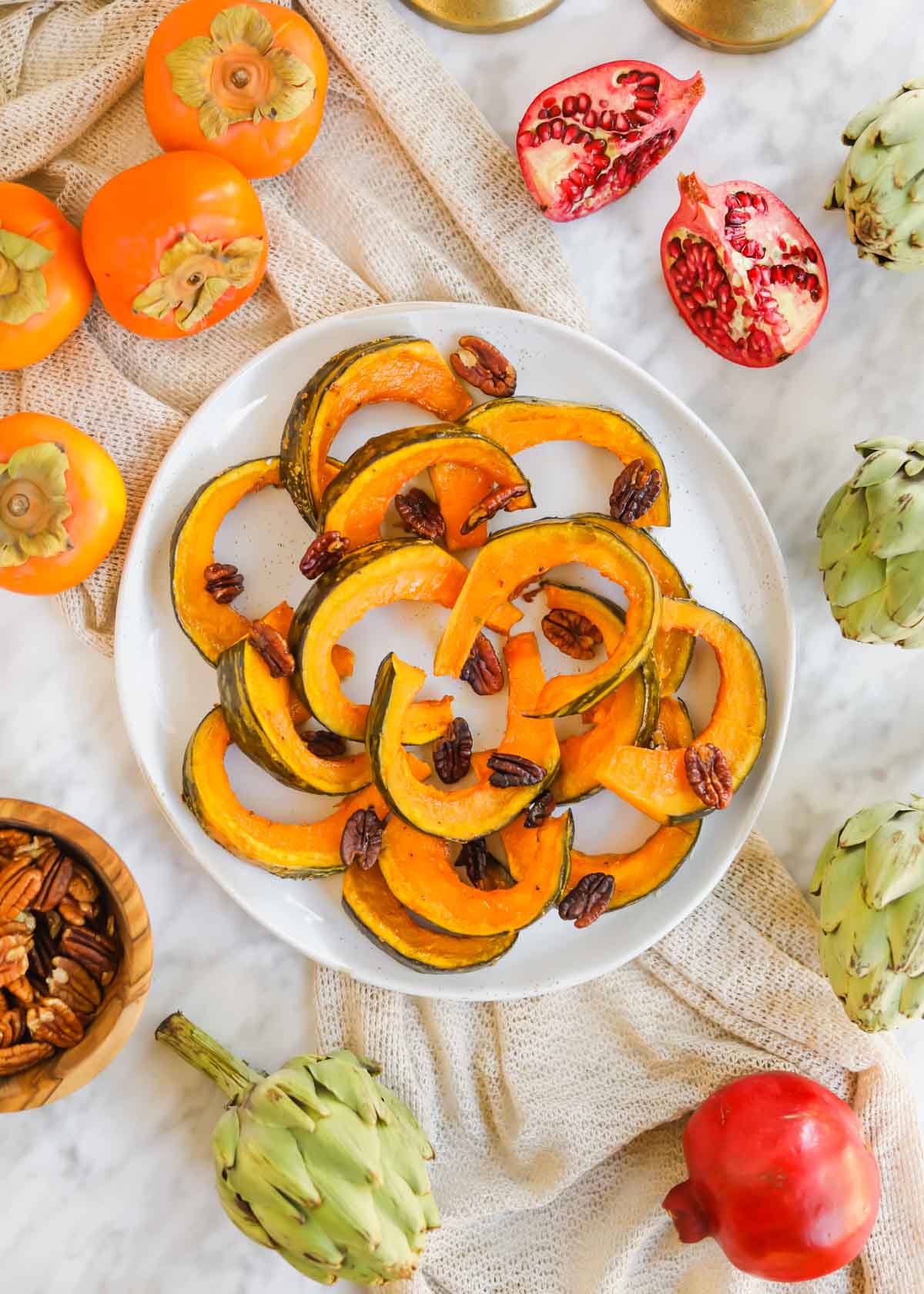 Maple Roasted Kabocha on plate surrounded by artichokes,  pecans, pomegranates, and persimmons.