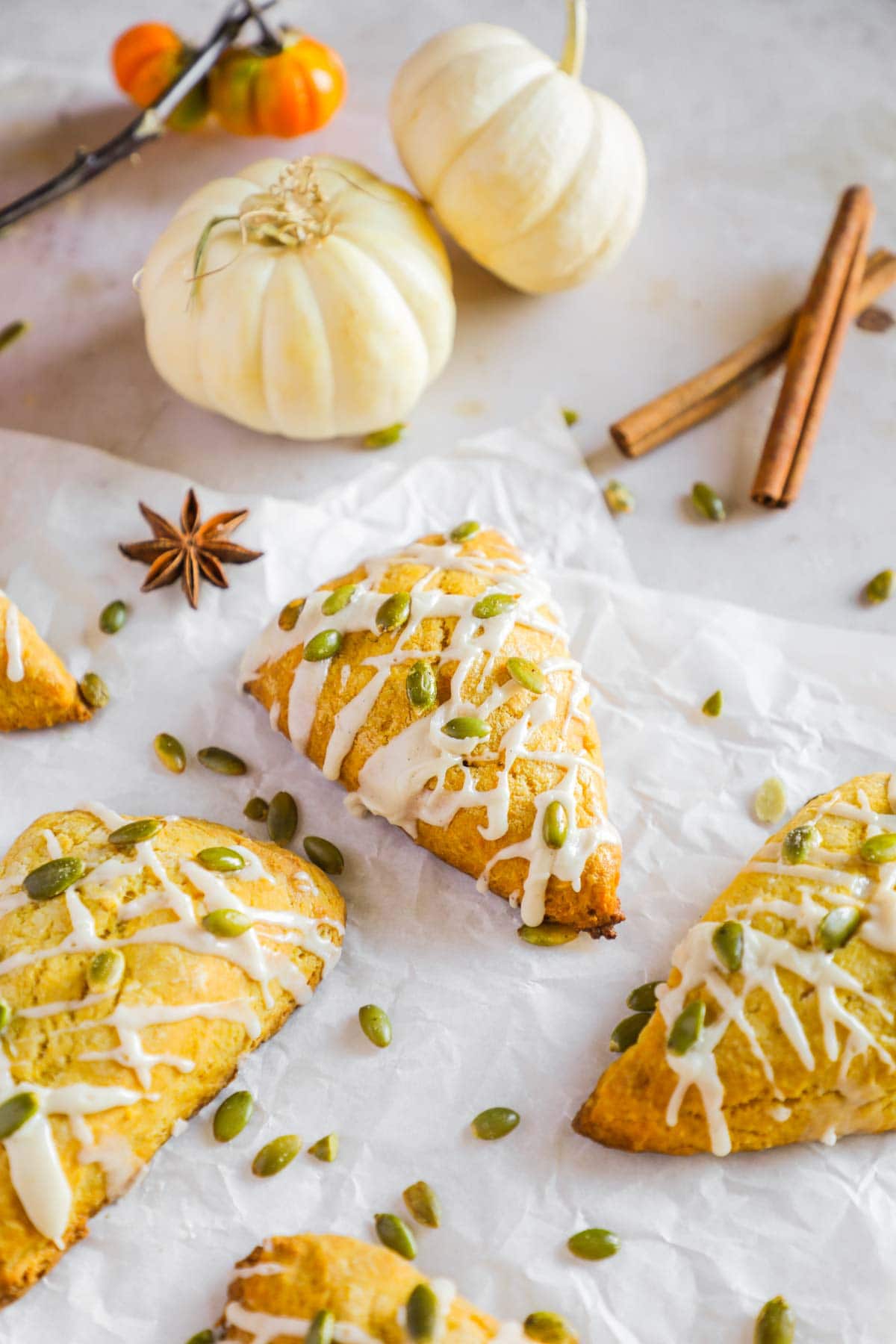 Pumpkin scones (better than Starbucks!) with maple vanilla paste glaze on parchment paper with decorative white pumpkins and cinnamon sticks.