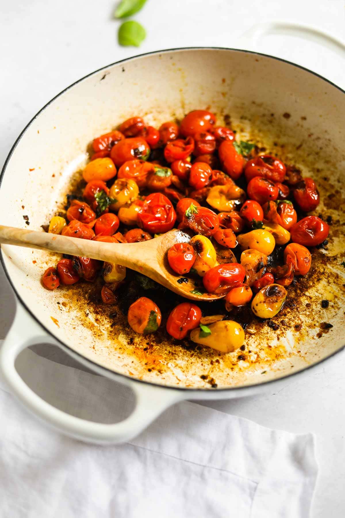 Blistered cherry tomatoes in a white Le Creuset braiser with a wooden spoon