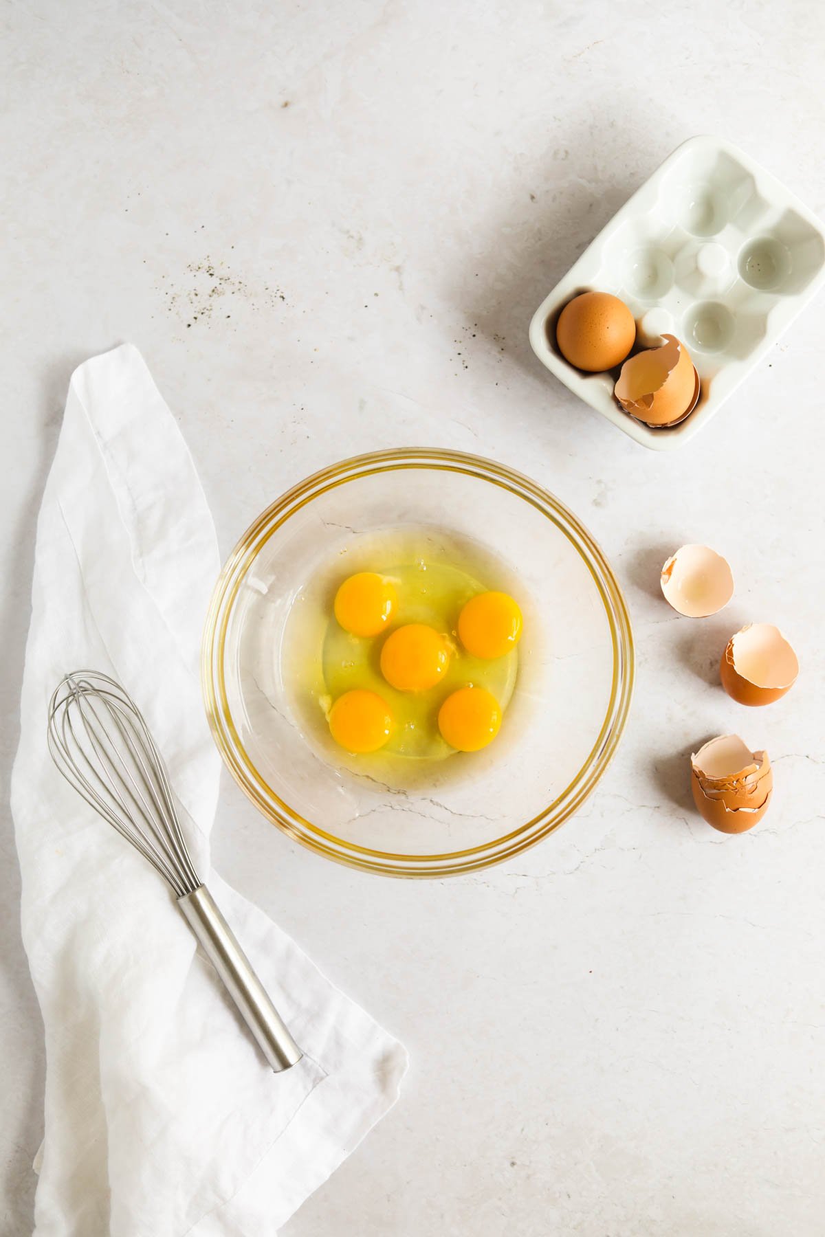 pasture-raised eggs in a glass mixing bowl with a stainless steel whisk. Eggs in a white egg carton