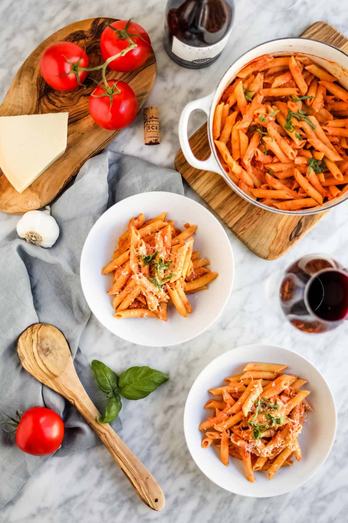 Penne pasta with vodka sauce in white bowls and dutch oven with wine, basil, garlic, tomatoes and cheese.