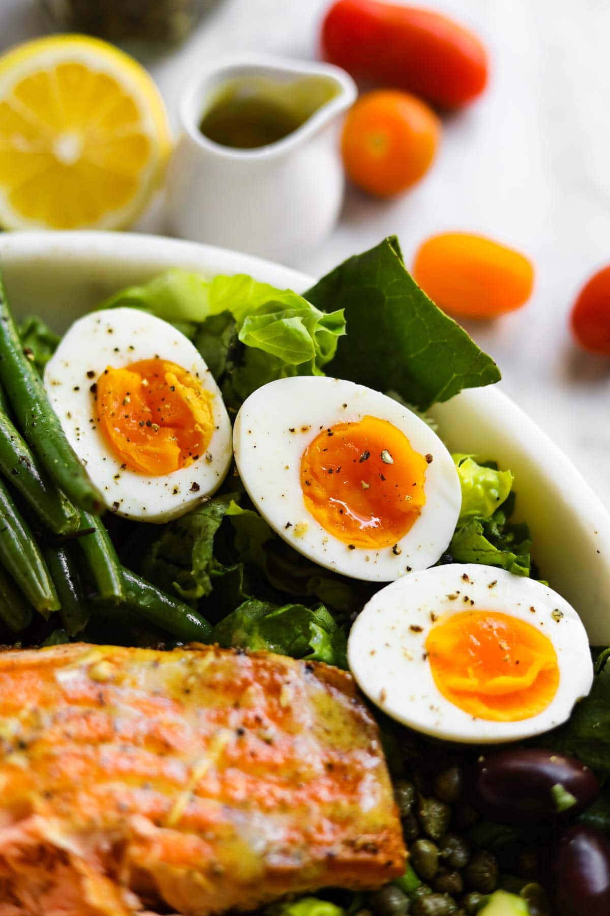 Soft Boiled Jammy Eggs in a salad bowl with tuna and lemon, tomatoes, and dressing in background.