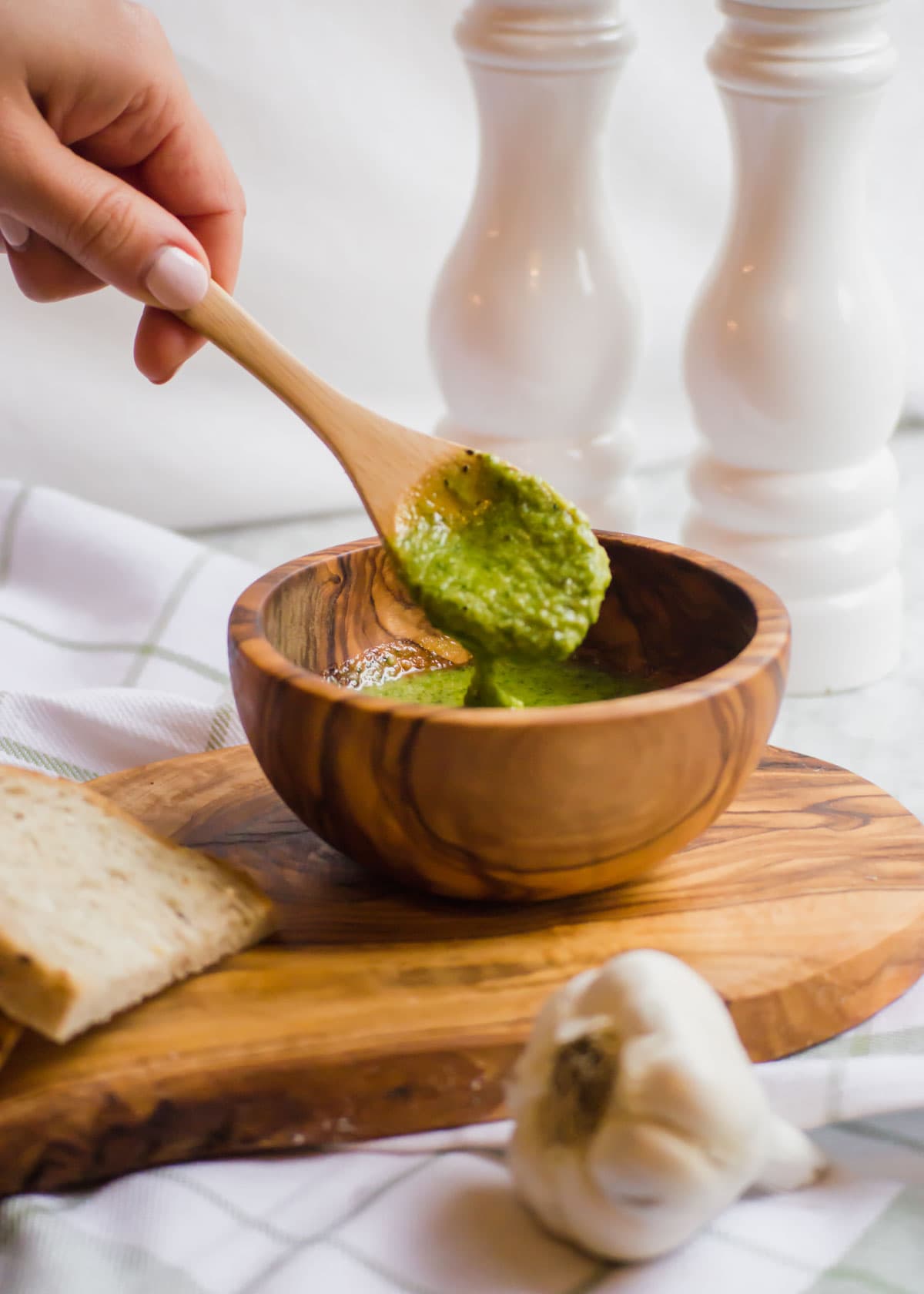 Wooden spoon with pesto above bowl.