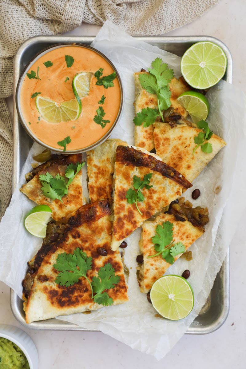 Cheese Quesadilla on a sheet pan with parchment paper, sliced limes, cilantro, and a bowl of chipotle lime mayo sauce.