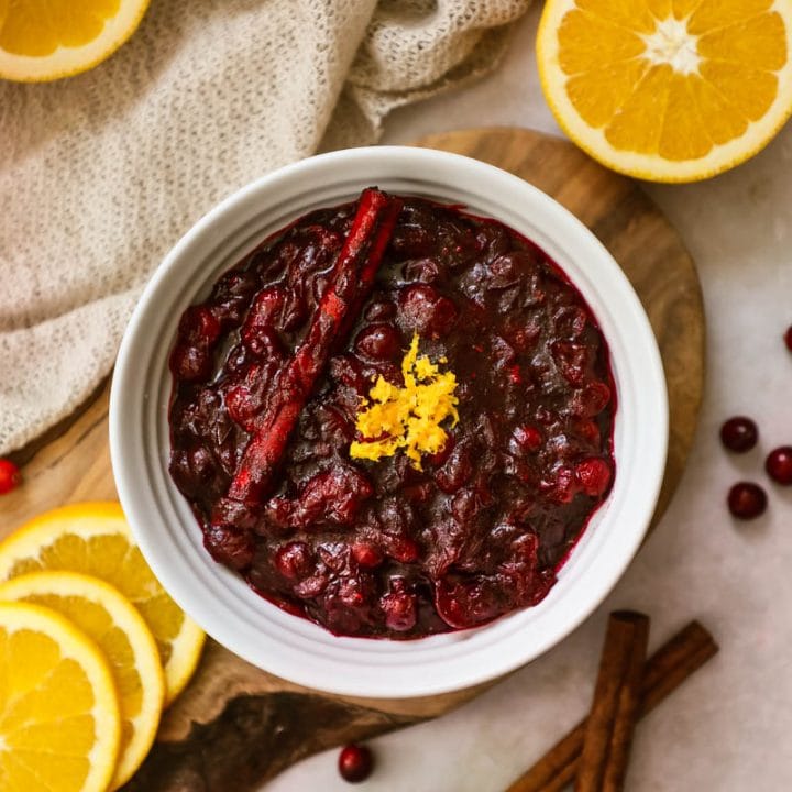 Cranberry sauce with cinnamon sticks and orange zest in a white bowl.