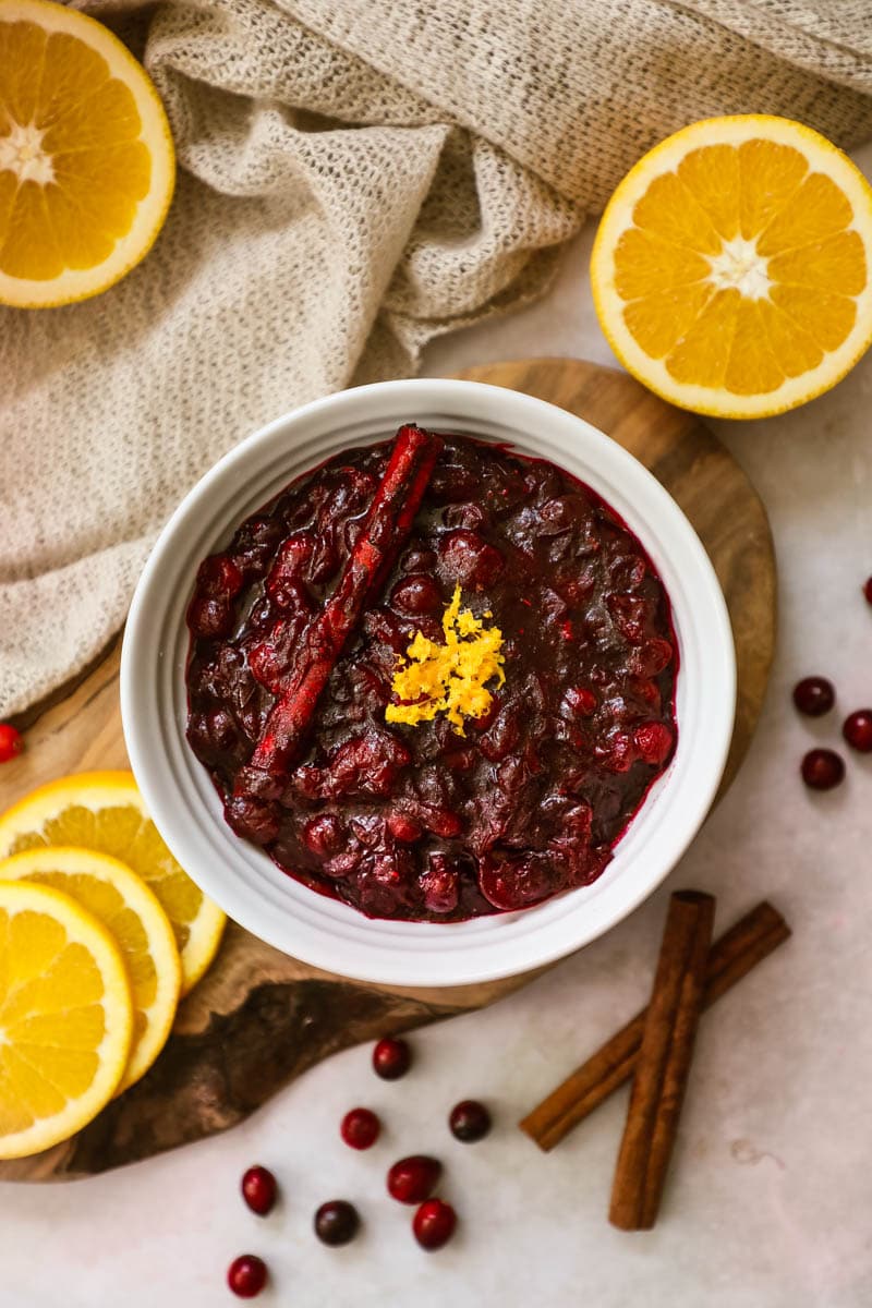 Cranberry sauce with orange zest and cinnamon sticks in a white serving bowl.