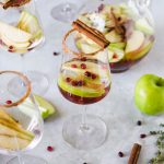 Fall sangria with pumpkin spice, apple, cinnamon sticks, and pomegranate seeds in a glass and a large glass pitcher.
