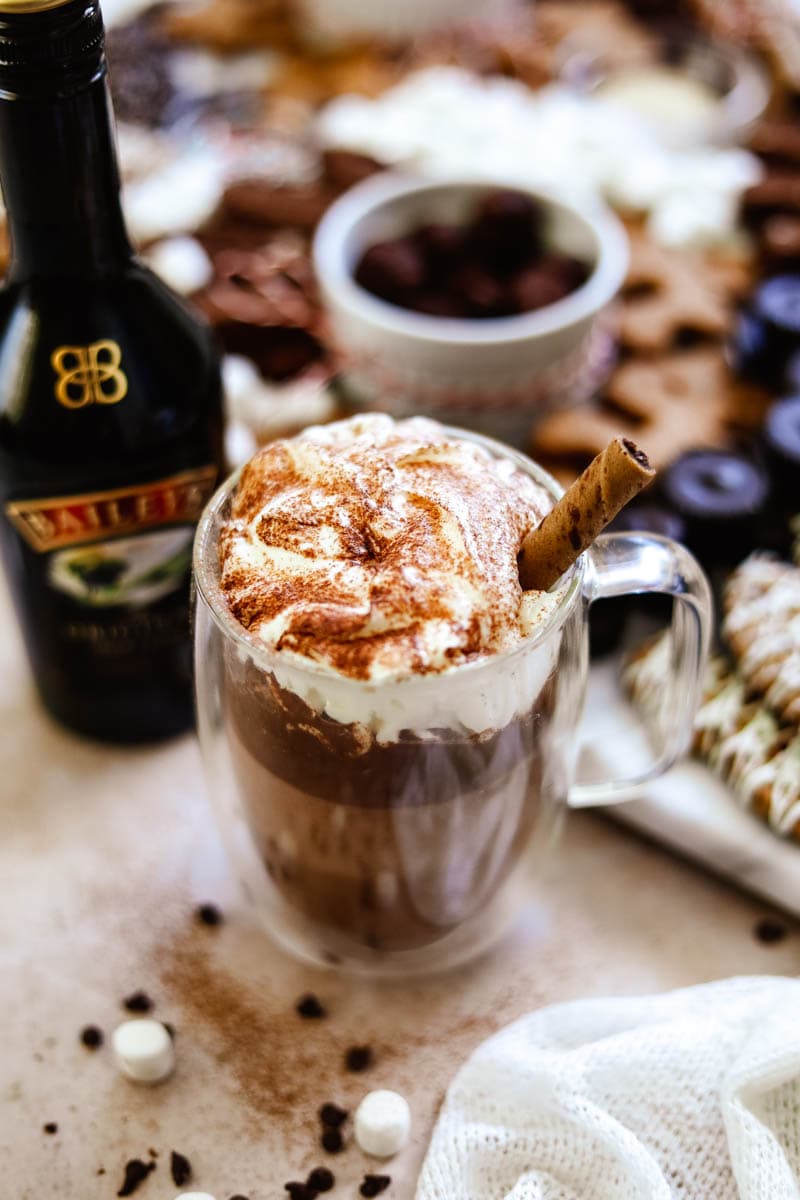 Baileys Hot Chocolate in double-wall glass mugs, whipped cream, cocoa powder, and a pirouette wafer cookie.