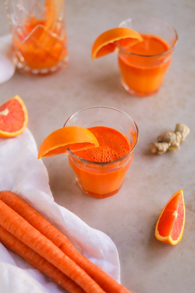 Freshly juiced Carrot Orange Ginger Juice in a Duralex glass with an orange wedge.
