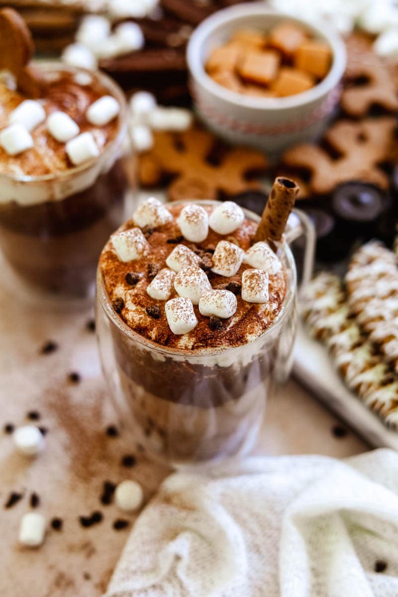 Oat milk hot chocolate with vegan whipped cream, vegan marshmallows, cocoa powder, and a pirouette creme wafer cookie.
