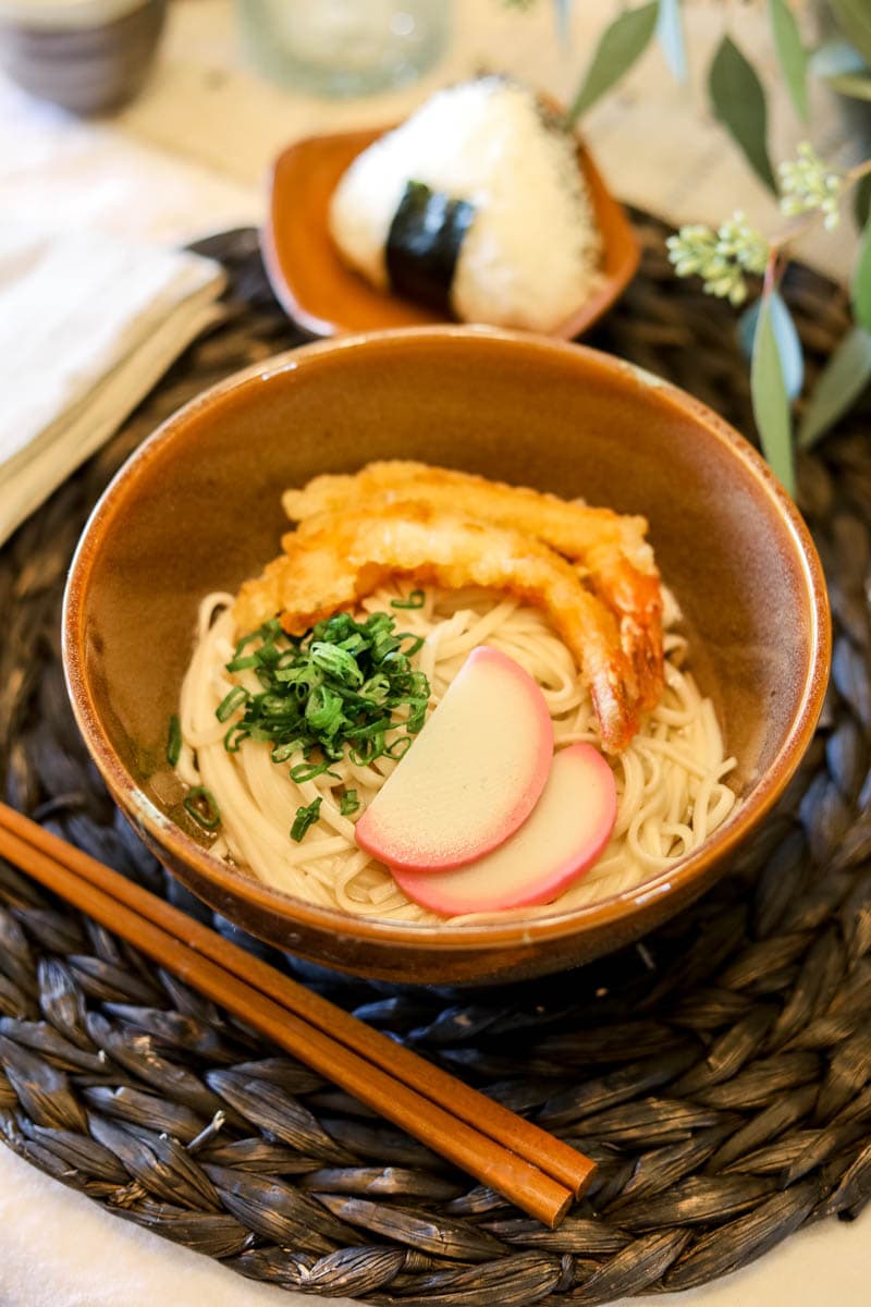 Shrimp Tempura Udon in a bowl with kamaboko, sliced green onions, and dashi.