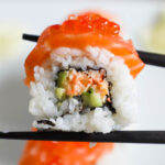 Closeup shot of Alaska sushi roll with Ikura held with chopsticks.