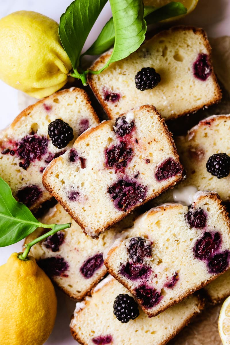 Blackberry lemon bread loaf cut into slices surrounded with real lemons and lemon zest icing.