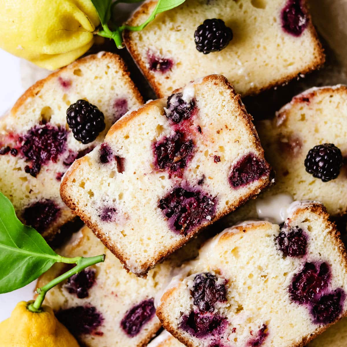 Blackberry lemon bread loaf cut into slices surrounded with real lemons and lemon zest icing.