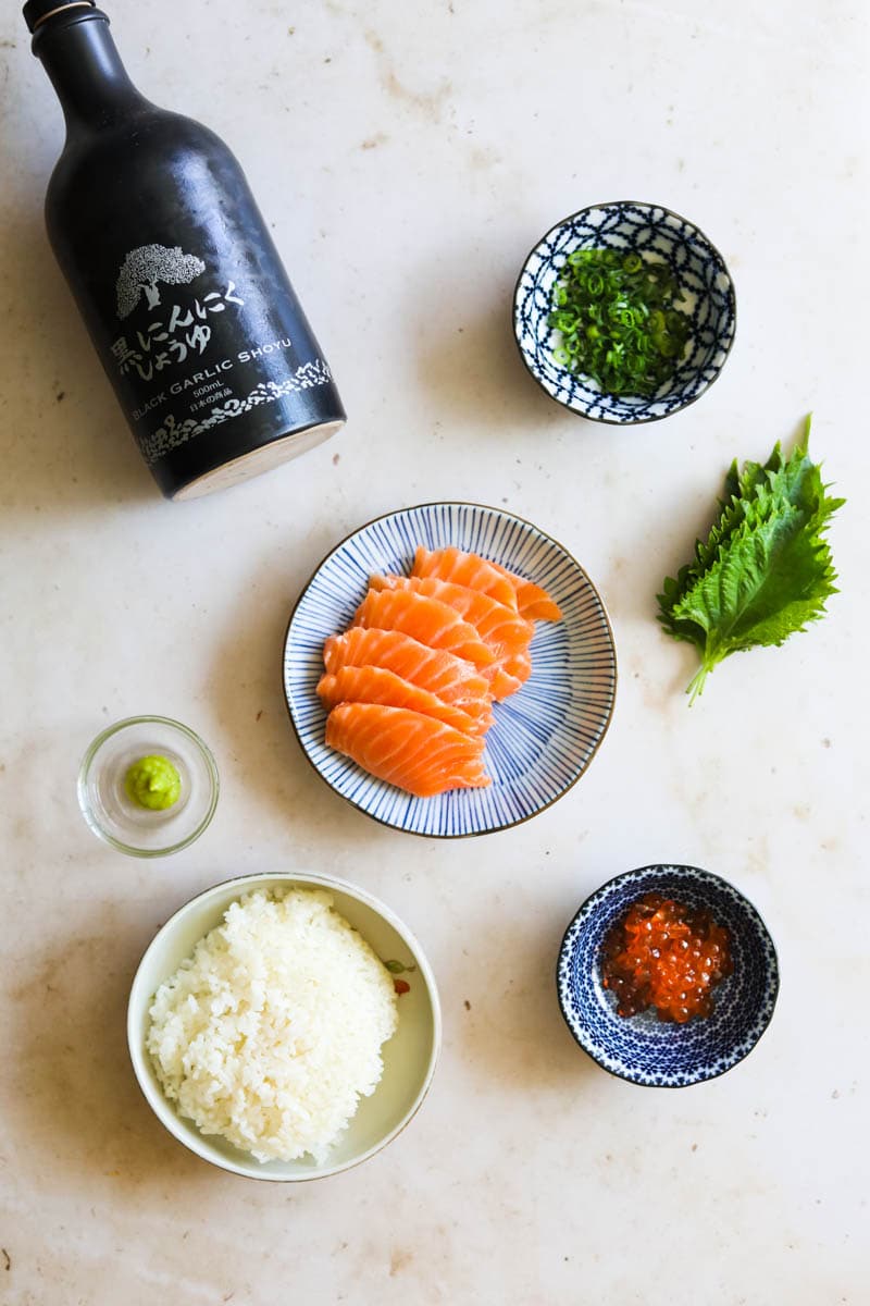 Ingredients to make salmon sashimi donburi with shiso, rice, Ikura, scallions, wasabi, and soy sauce.