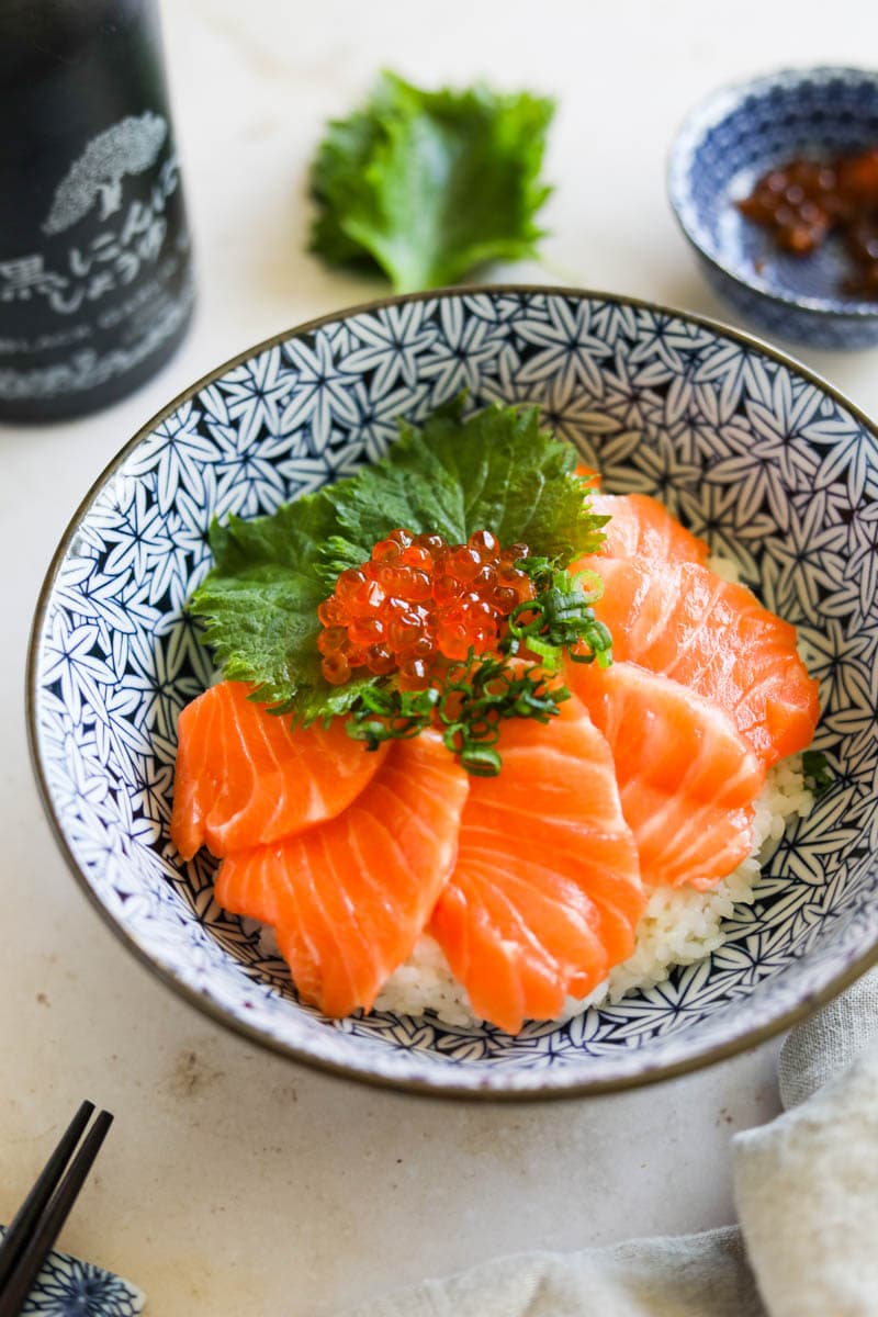 Salmon sashimi donburi with shiso, Ikura, and scallions in a blue and white bowl.