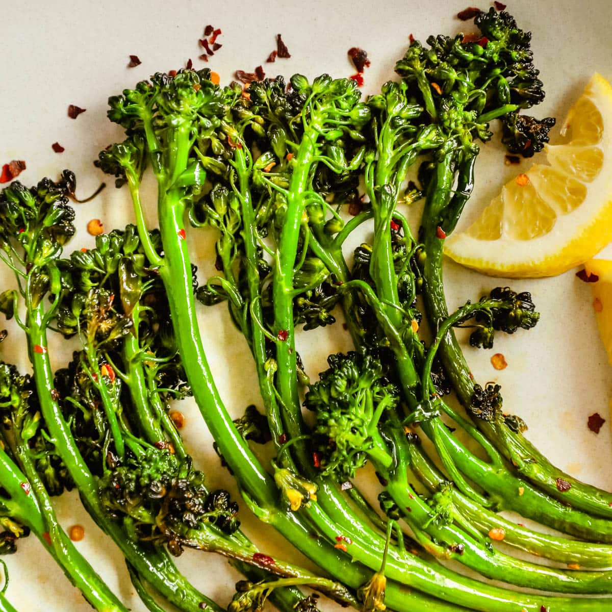 Closeup of easy delicious charred broccolini/broccoletti on a plate with seasoning, lemon wedges, and chili flakes.