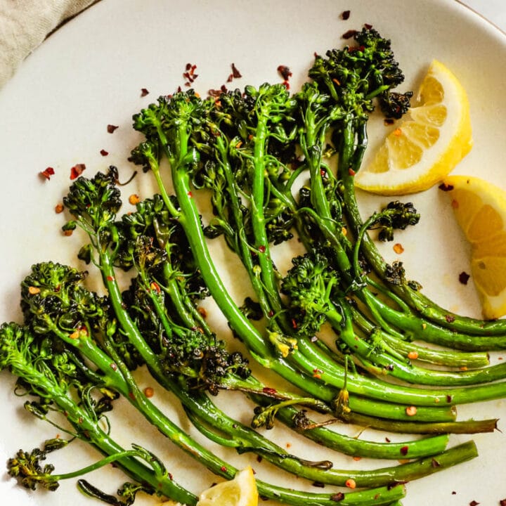 Easy delicious charred broccolini/broccoletti on a plate with seasoning, lemon wedges, and chili flakes.