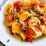 Closeup shot of Calamarata calamari and tomato pasta in a white bowl.