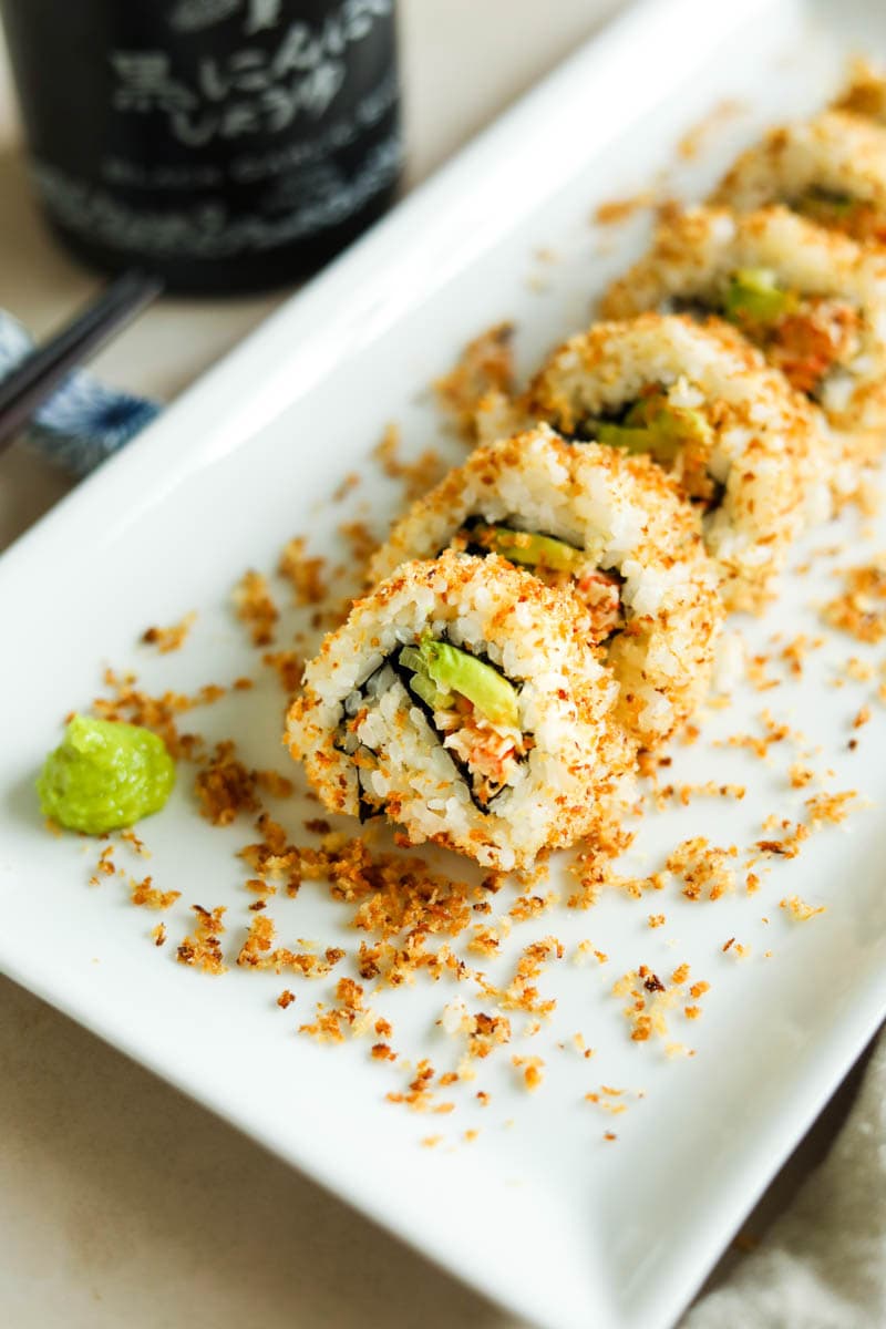 Spicy Crunchy California sushi roll tossed in a crispy panko crust on a white plate with wasabi.