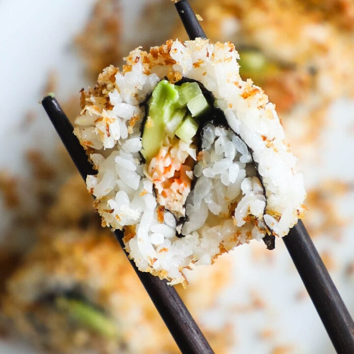 Closeup shot of crunchy spicy California sushi roll in chopsticks.