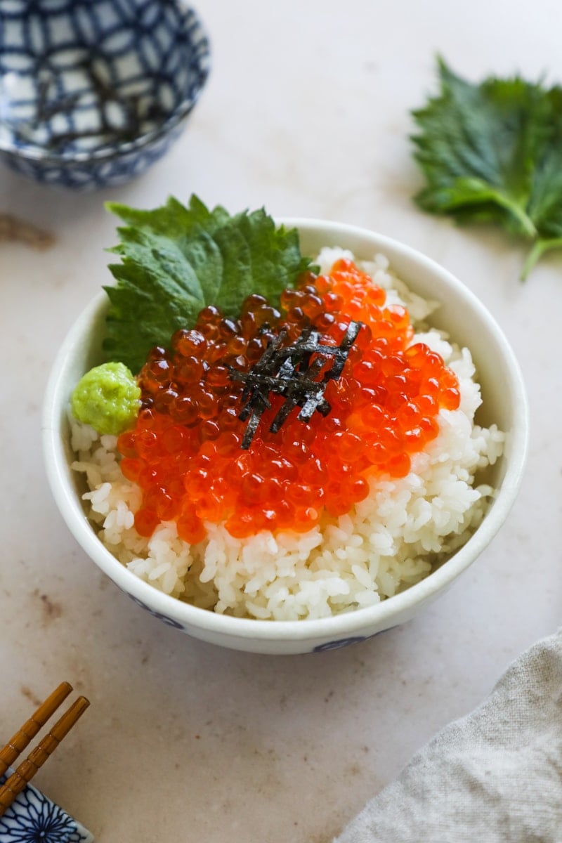 Ikura salmon roe on a bed of rice with shiso leaf and wasabi in a donburi bowl.