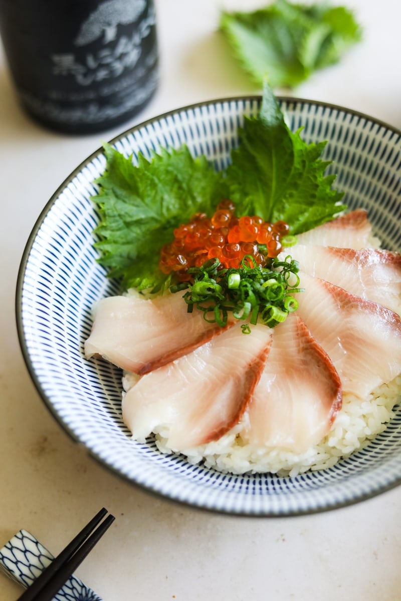 Closeup of yellowtail sashimi (hamachi donburi) in a bowl with rice, shiso, ikura, and scallions.