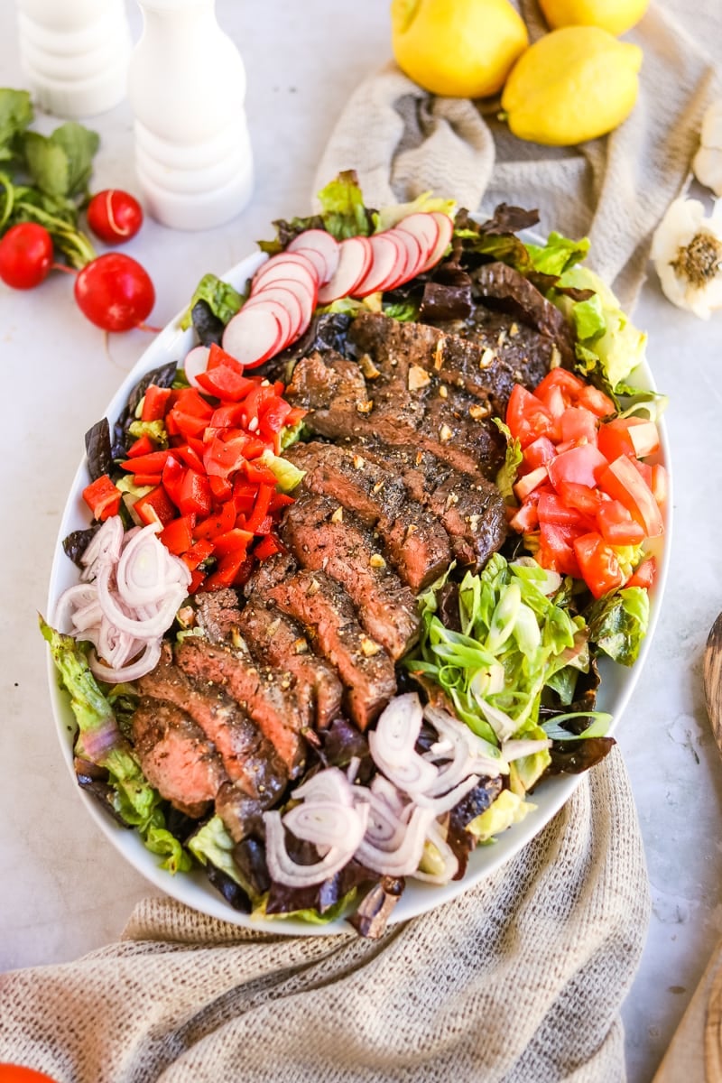 Flank steak salad with lettuce, radish, tomato, bell pepper, shallot, green onion, and a balsamic dressing.