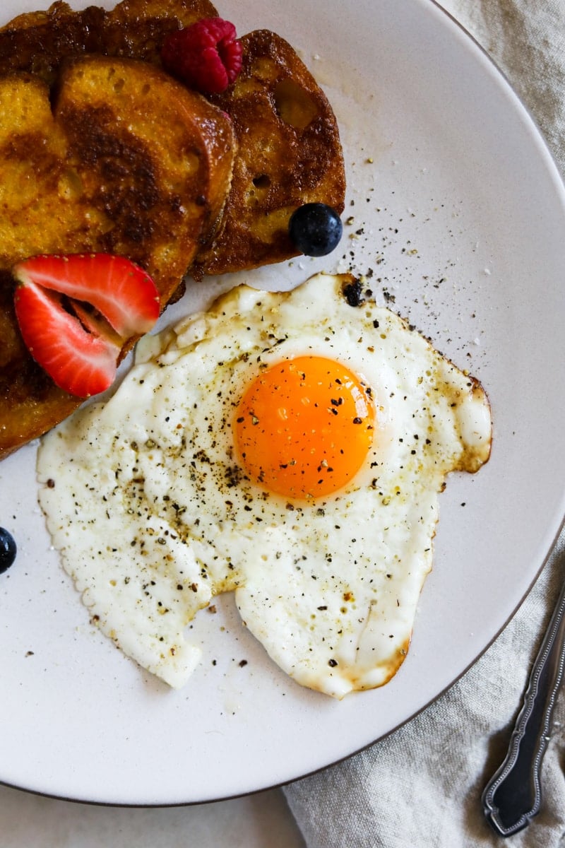 Sunny side egg with salt and pepper on a plate with sourdough French toast and berries.