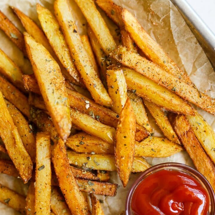 Classic seasoned french fries with garlic powder, dried basil, paprika, and ketchup on a baking sheet with parchment paper.