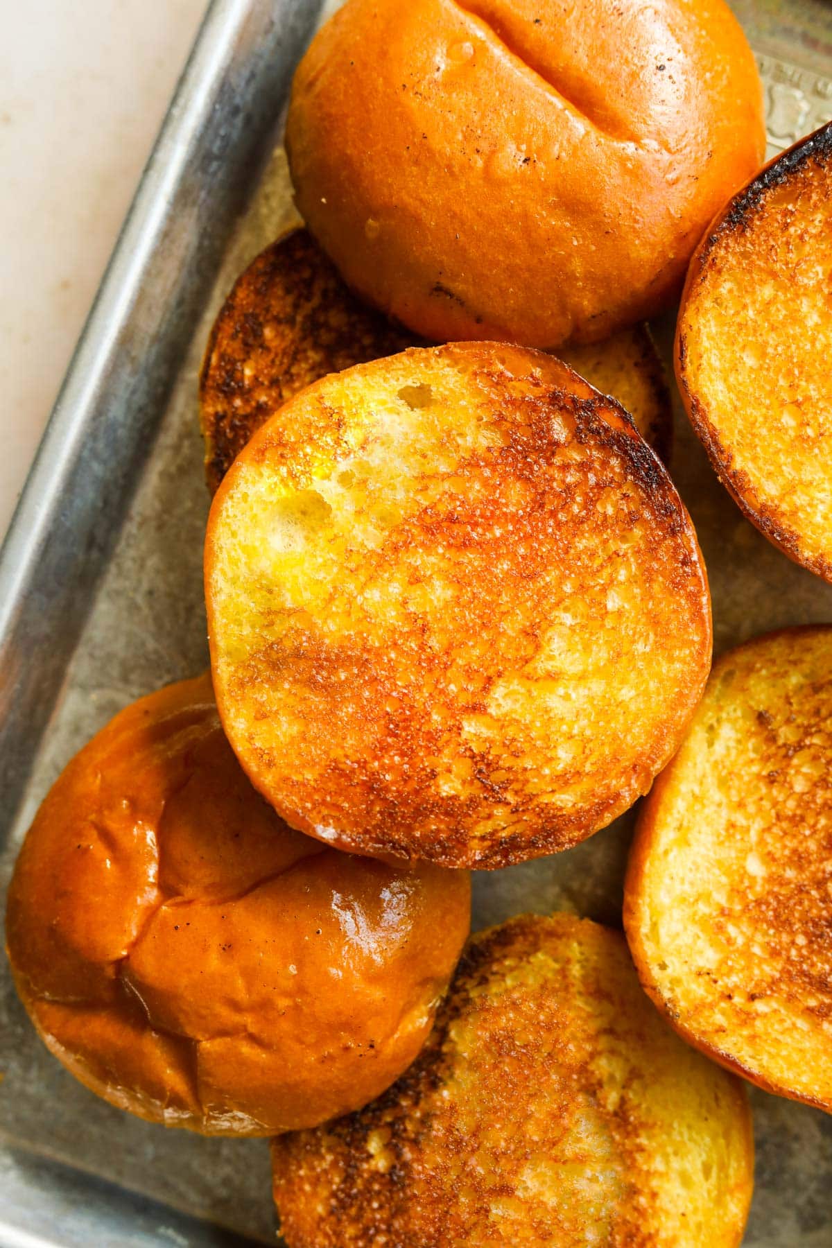 Up-close shot of golden toasted brioche burger buns on a baking sheet.