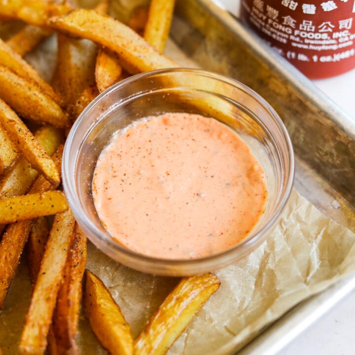Spicy sriracha aioli in a bowl with French fries and a bottle of sriracha.