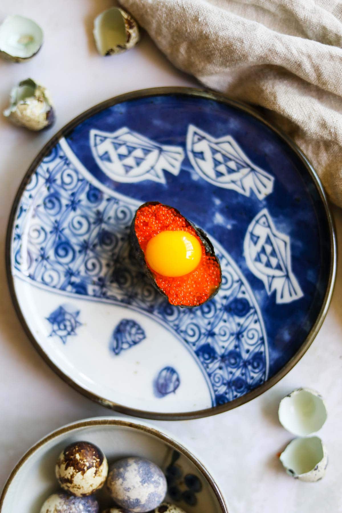 Overheard flatlay shot of roe quail egg gunkan sushi on a blue Japanese plate.