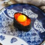 Tobiko quail egg gunkan sushi on a blue Japanese ceramic plate.